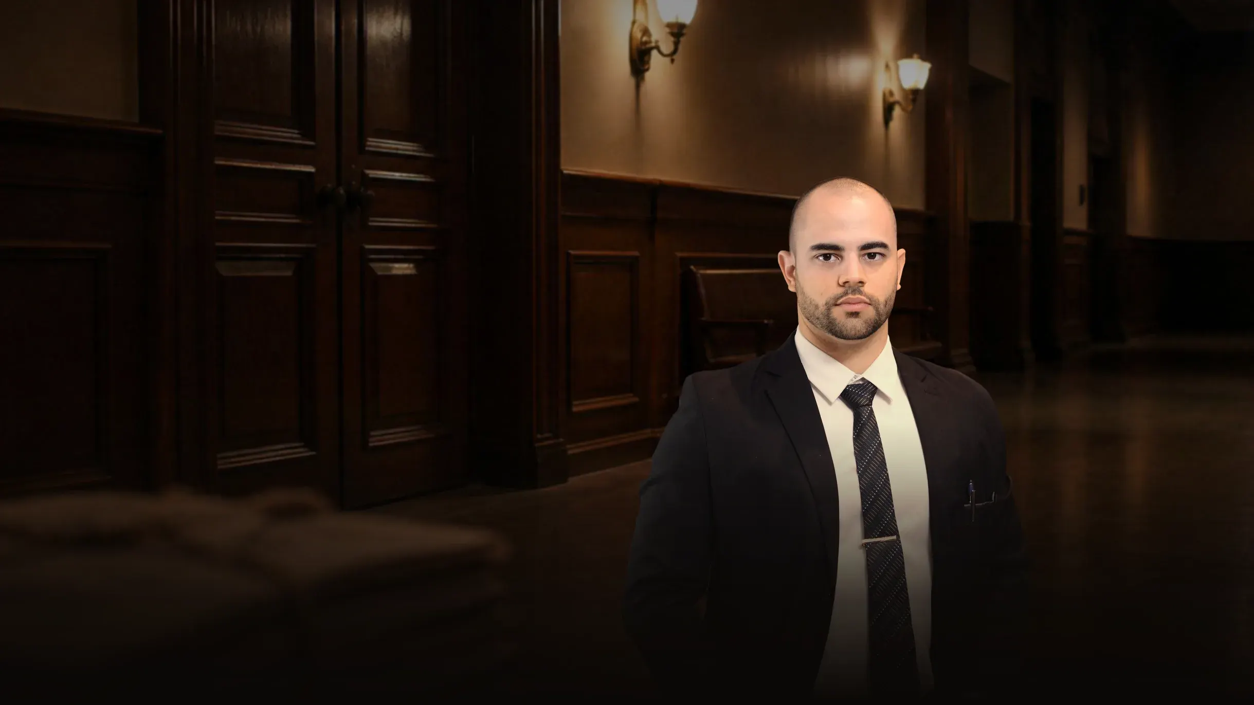 Renan Gaudereto Teixeira, advogado em audiência de custódia, em pé no corredor do fórum, diante das portas de uma sala de audiência