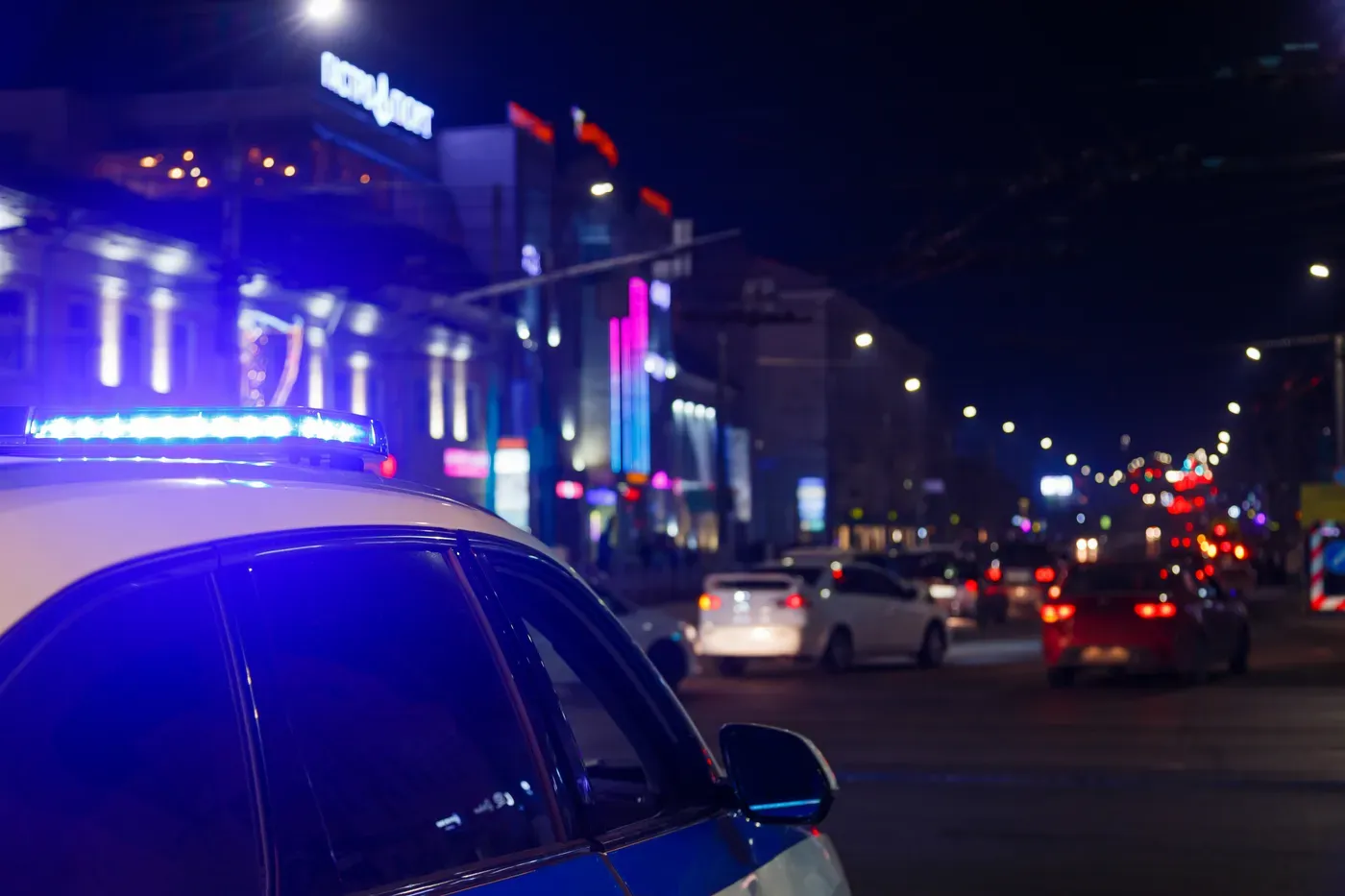 Giroflex azul aceso no teto de uma viatura da polícia, numa rua da cidade à noite, com o trânsito desfocado ao fundo