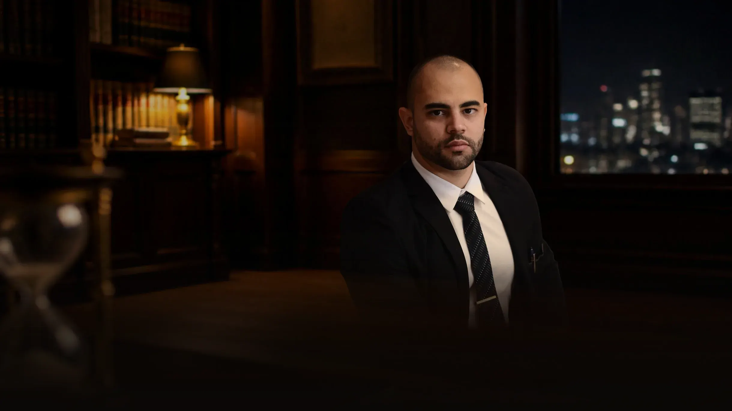 Renan Gaudereto Teixeira, advogado criminalista, sentado no escritório à noite, com a cidade iluminada pela janela ao fundo