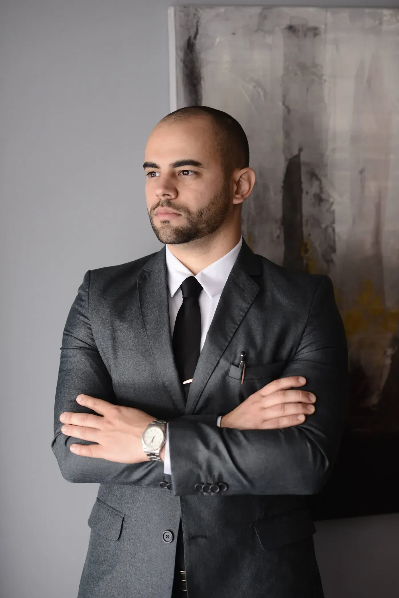 Renan Gaudereto Teixeira, advogado para estelionato e crimes financeiros, de braços cruzados diante de uma parede cinza, olhando para o lado
