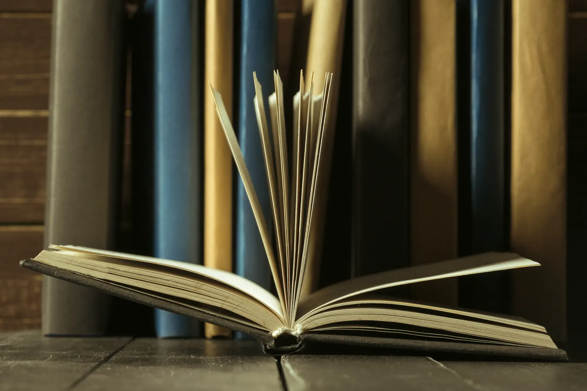 Livro aberto sobre uma mesa de madeira, diante de uma estante de livros de direito