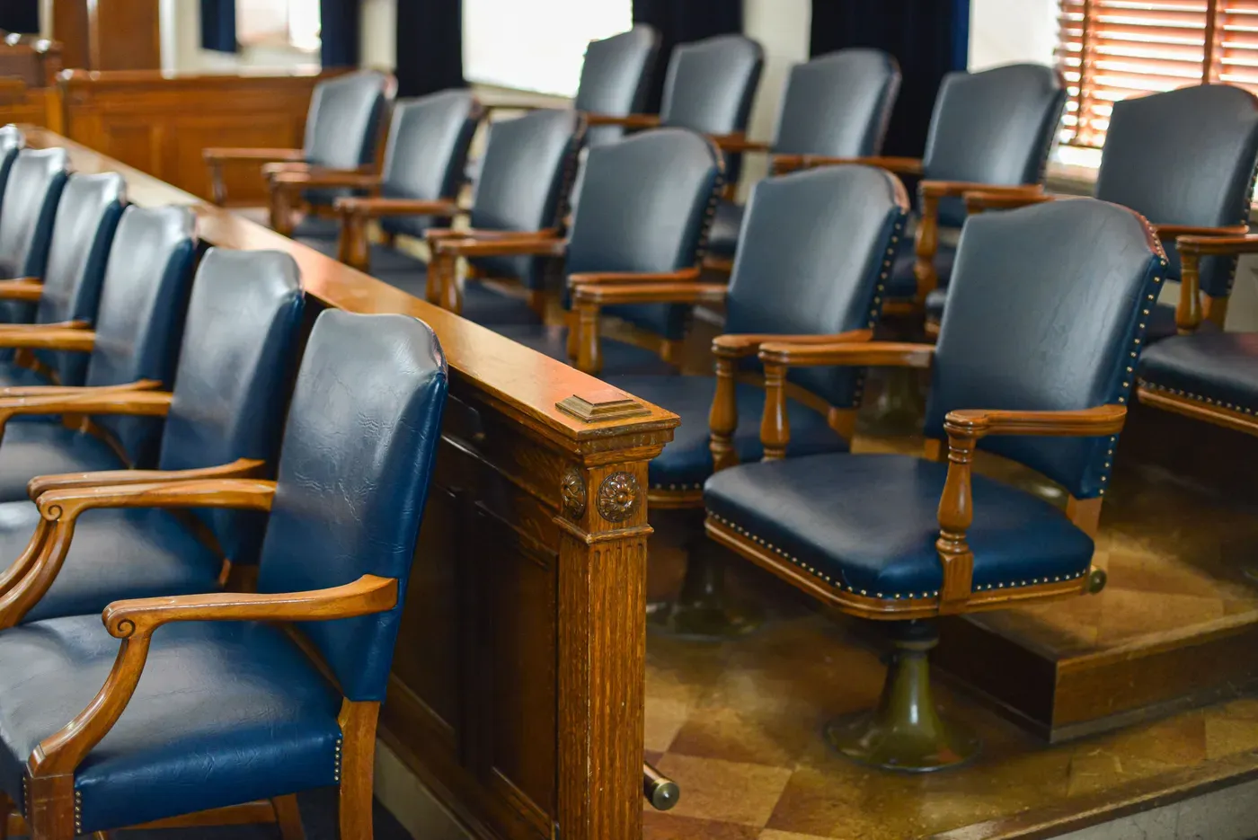 Cadeiras vazias da bancada dos jurados no plenário de um tribunal, com uma grade de madeira à frente