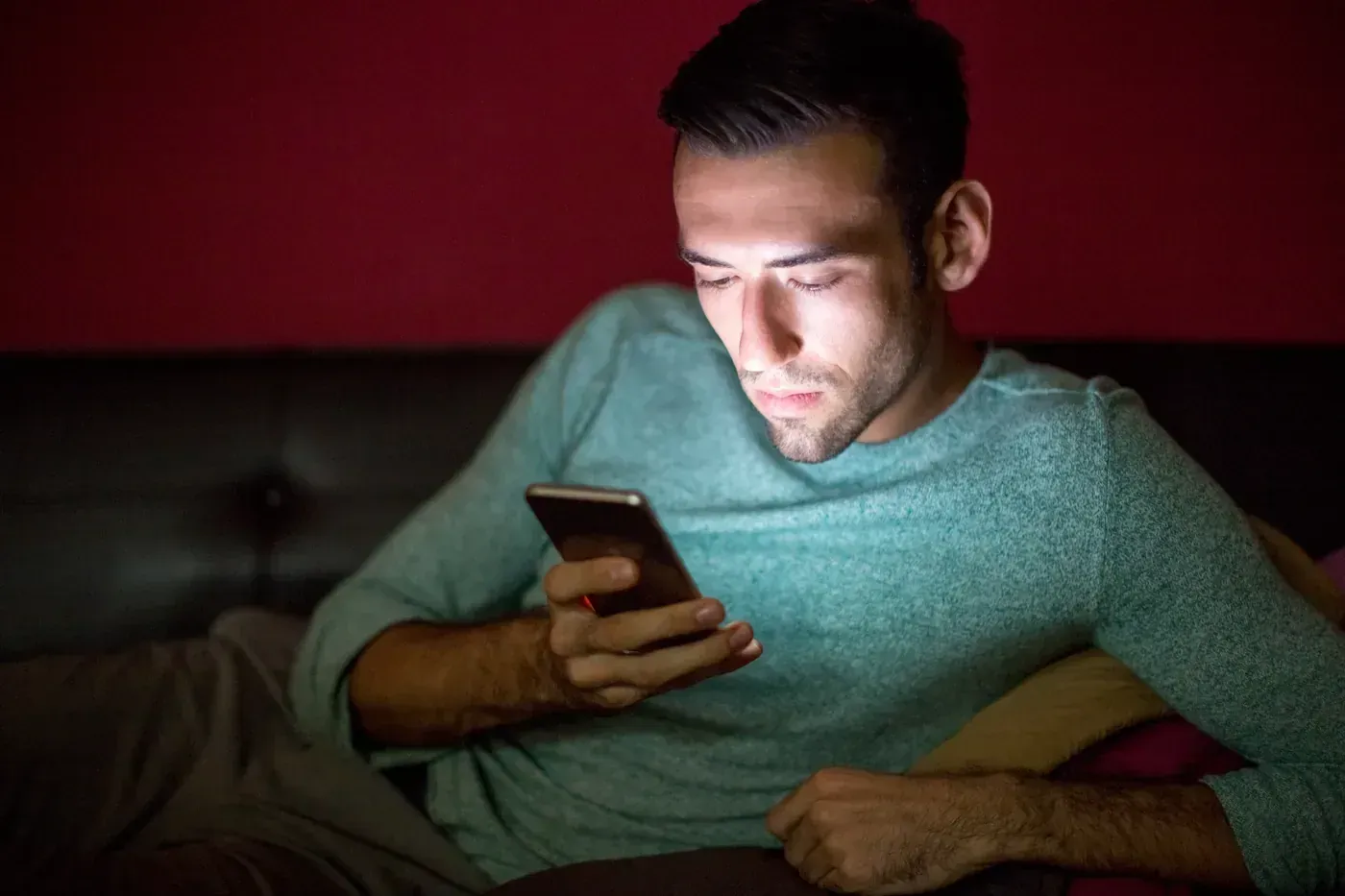 Homem sozinho no sofá à noite, segurando o celular com a tela acesa