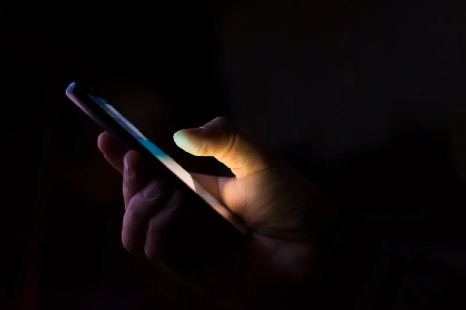 Mão segurando um celular aceso num ambiente escuro