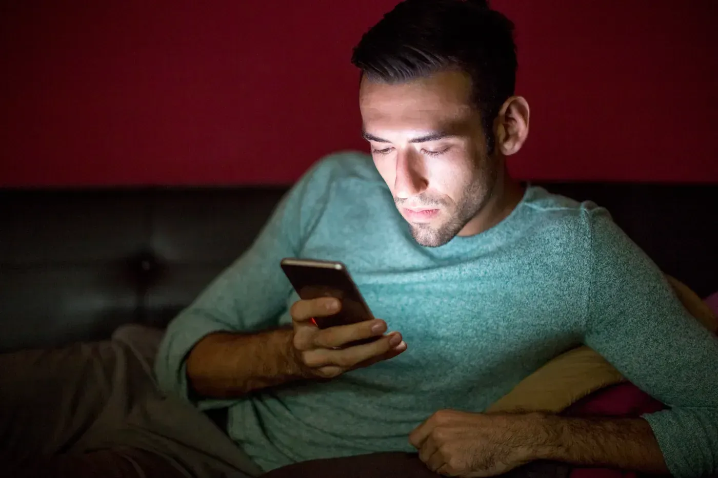 Homem sentado no sofá à noite, com o rosto iluminado pela tela do celular