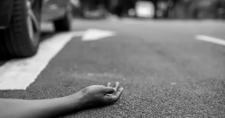 Mão de uma pessoa caída no asfalto ao lado de um carro