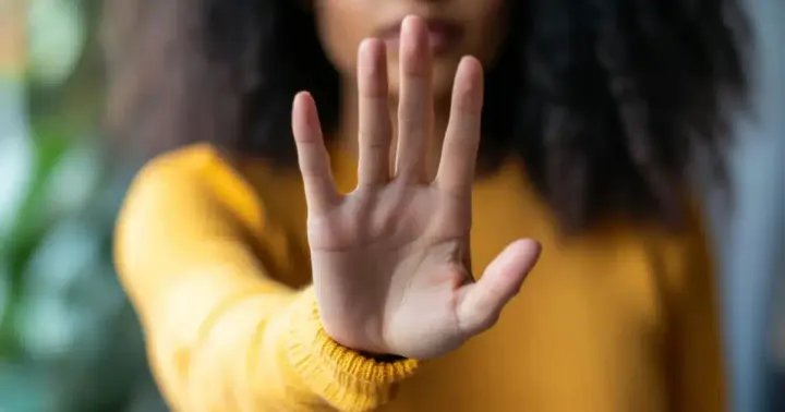 Mulher de blusa amarela estende a mão aberta em sinal de pare